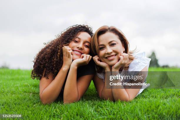 jonge moeder en dochter die op gras liggen dat camera onder ogen ziet die terwijl het leunen van hun gezicht op handen glimlacht - woman smiling facing down stockfoto's en -beelden