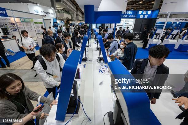 Visitors look at screens displaying Japanese company Tomorrow Net's navigation-type AI communication tool "CAT.AI" with a ChatGPT function during the...