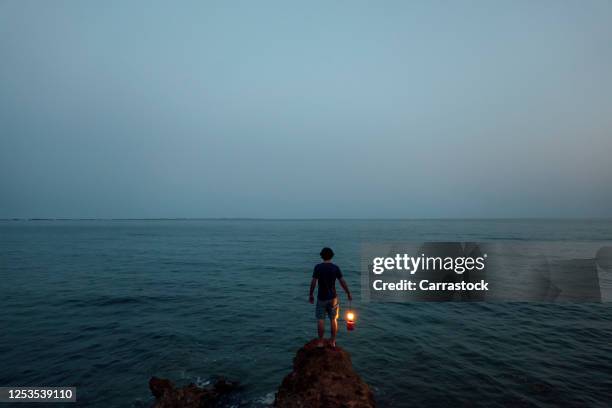 a person with a lantern by the sea - desorientiert stock-fotos und bilder