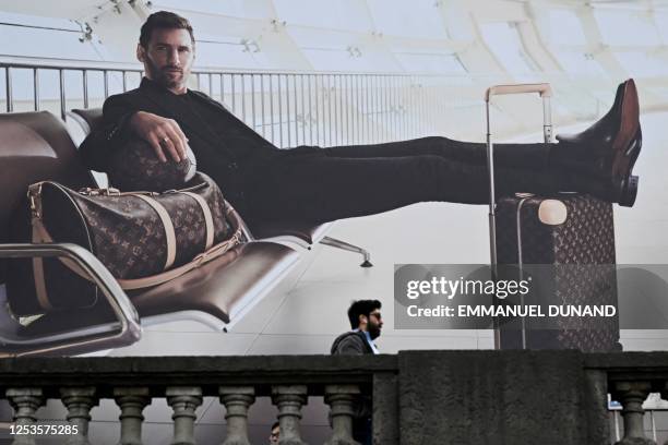 Pedestrian walks past a poster add with Argentinian football player Lionel Messi posing with luggages for Louis Vuitton brand, in front of the Musee...