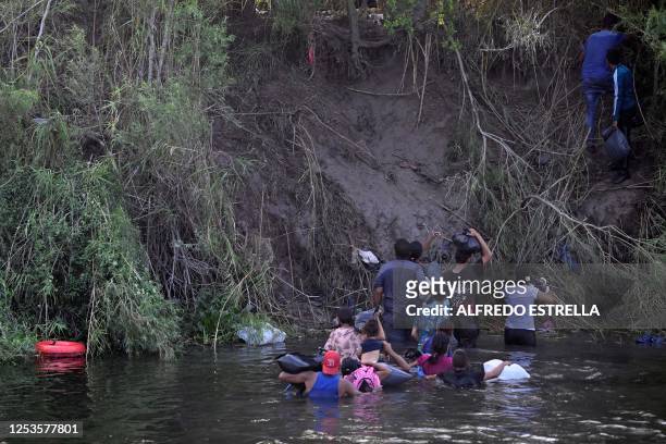 Migrants cross the Rio Bravo river as members of the US National Guard reinforce a barbed-wire fence along the US-Mexico border river, as seen from...