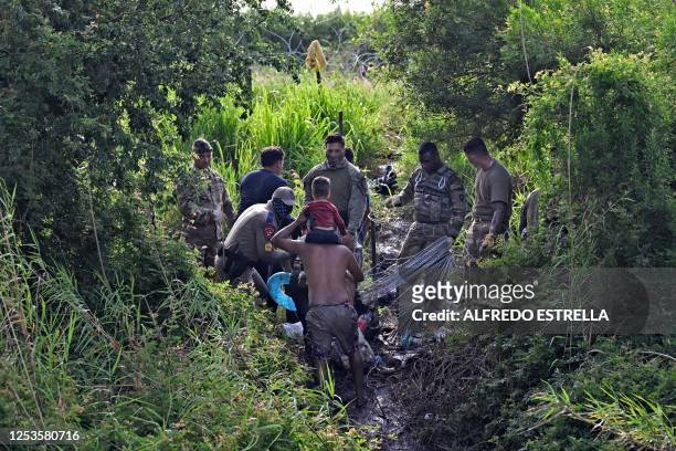Migrants who crossed the Rio Bravo river try to go through as members of the US National Guard reinforce a barbed-wire fence along the US-Mexico...