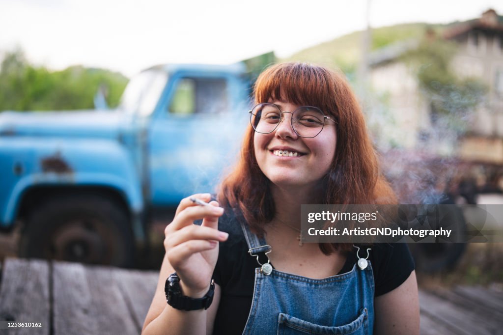 Retrato de una mujer joven sonriente fumando marihuana al aire libre.