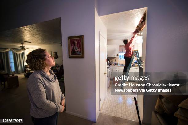 Michelle Toy, left, watches from the living room as Hannah Siqueiros, of HT Innovations, clears insulation from the ceiling after a broken pipe was...