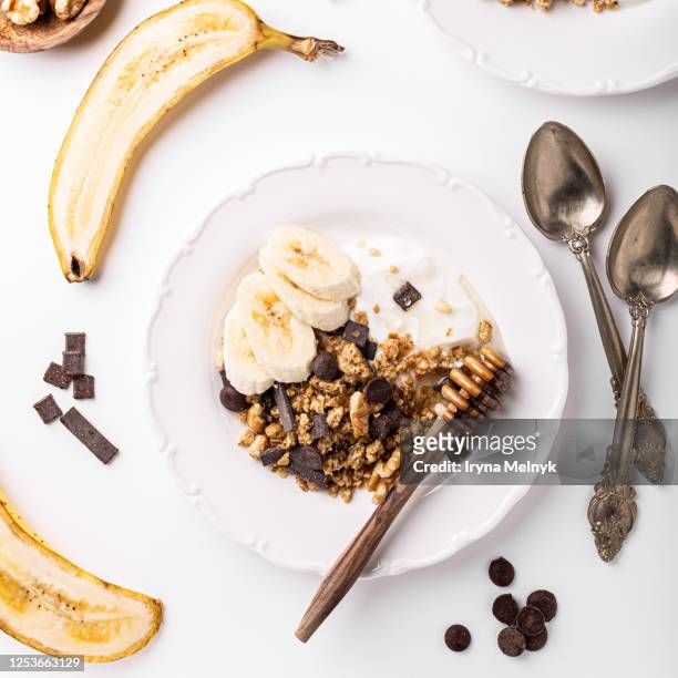 healthy breakfast with homemade granola with nuts mix, yogurt, chocolate pieces, banana and honey on white plates, top view. - haferflocken stock-fotos und bilder
