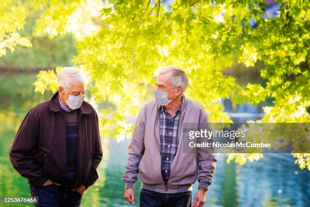 couples masculins aînés gais utilisant des masques protecteurs pendant la promenade d’automne dans le parc - fall prevention photos et images de collection