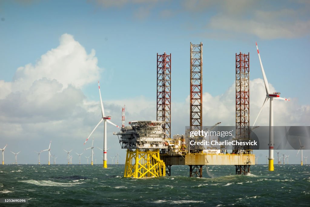 Vista épica em Grandes turbinas eólicas offshore 8MW, parque eólico no horizonte no mar do Norte com barco jack up e plataforma offshore em mar ondulado