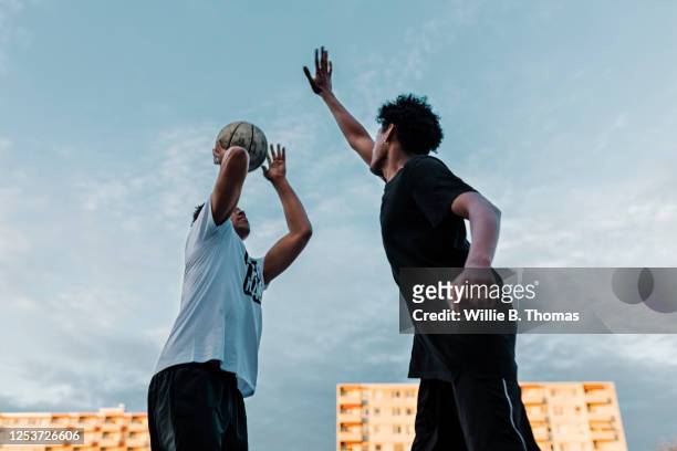 friends playing one on one basketball game - leben in der stadt stock-fotos und bilder