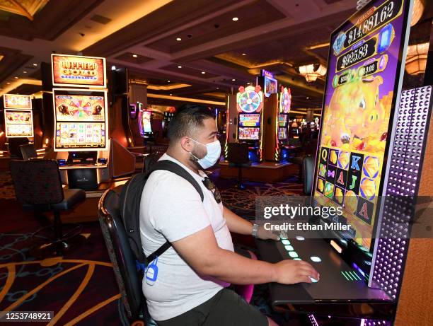 Jose Medina of Texas wears a mask as he plays a slot machine at Mandalay Bay Resort and Casino after the Las Vegas Strip property opened for the...