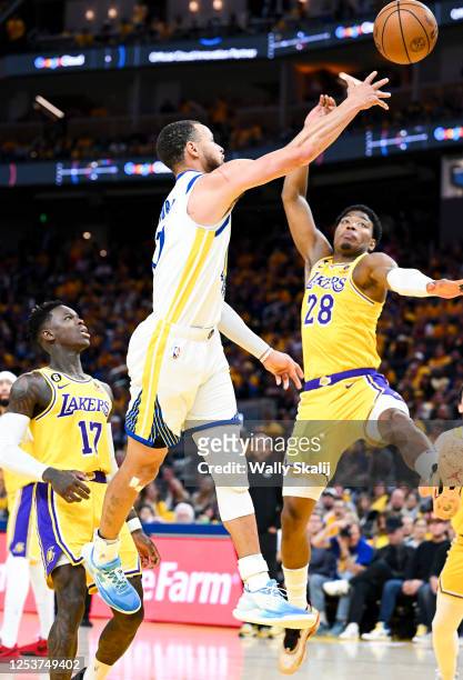 Golden State Warriors guard Stephen Curry, center, jumps past Los Angeles Lakers guard Dennis Schroder, left, while passing the ball as forward Rui...