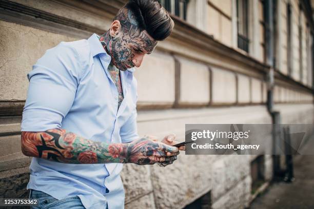 modern man with whole body covered in tattoos using phone on the street - handsome tattoo stock pictures, royalty-free photos & images