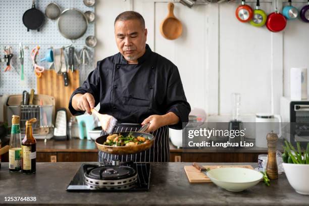 一個亞洲中年廚師在廚房烹飪 - asian man cooking bildbanksfoton och bilder