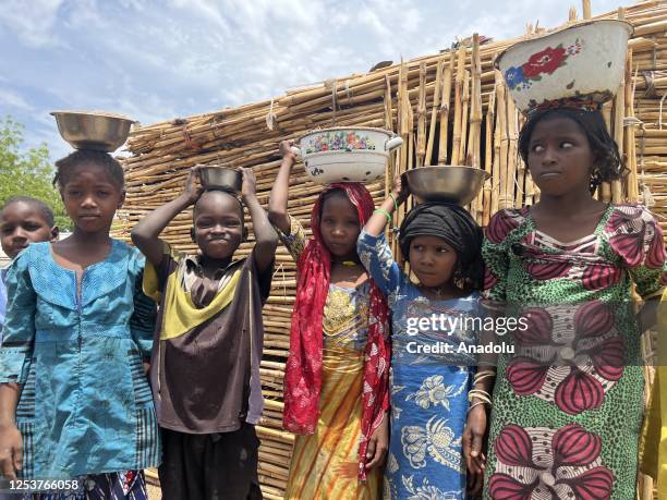 Nigerian children carry buckets of food on their heads at the Gwoza IDP Camp in Borno State, Nigeria on May 03, 2023. While the number of people...