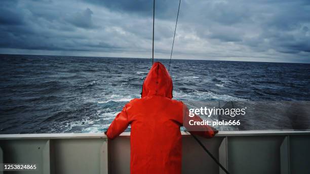 pêcheur regardant la mer sur le pont de bateau de pêche, avec un imperméable orange - ship photos et images de collection