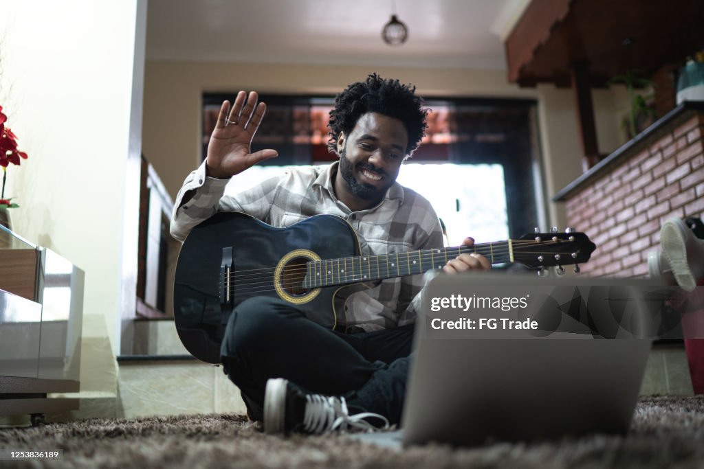 Enseñanza de guitarra acústica a través de una videollamada, saludando a la computadora portátil en casa