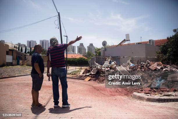 Israeli men stand near a scene where a rocket fired from the Gaza strip hit a house on May 11, 2023 in Ashkelon, Israel. One killed, 5 injured as...