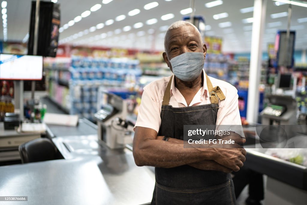 Afro senior hombre propietario de negocio / empleado con máscara facial en el supermercado