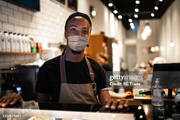 portrait of young waiter with face mask in coffee shop - shop reopening stock pictures, royalty-free photos & images