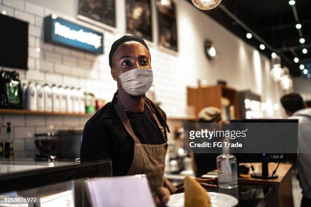 junge kellner mit gesichtsmaske arbeiten in café - essenzielle berufe und dienstleistungen stock-fotos und bilder