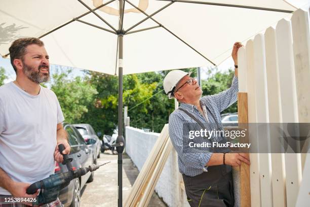 two men working on a construction site installing a wooden fence - fence installation stock pictures, royalty-free photos & images