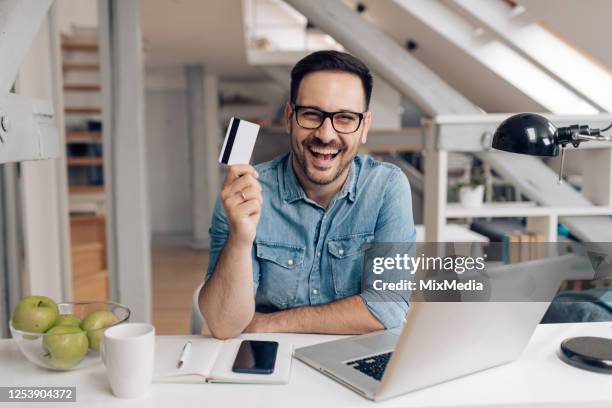 porträt eines glücklichen jungen mit kreditkarte im home office - mann mit kreditkarte stock-fotos und bilder