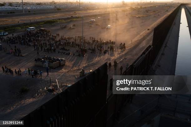 In this aerial picture taken on May 11, 2023 migrants line up to walk to board vans after waiting along the border wall to surrender to US Customs...