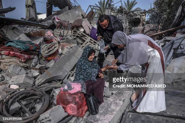 People assist a woman sitting amidst the rubble of a building hit in an Israeli air strike in Biet Hanoun, in the northern Gaza Strip, on May 12,...