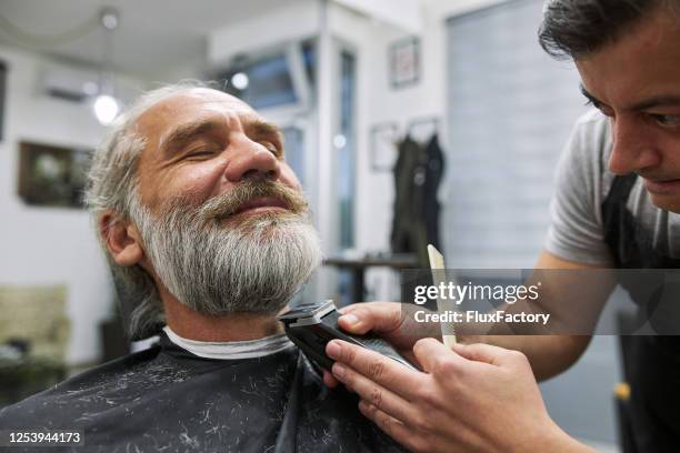 cheerful senior man relaxing while getting his beard cut - shave barber stock pictures, royalty-free photos & images