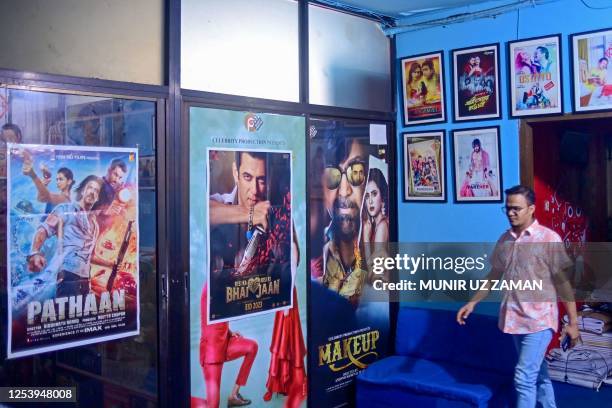 In this photograph taken on May 6 film distributor Anonno Mamun walks past posters of bollywood films 'Pathaan' and 'Kisi Ka Bhai Kisi Ki Jaan' at...
