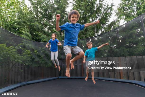 children jumping on a trampoline in a backyard without parents around - trampoline stock pictures, royalty-free photos & images