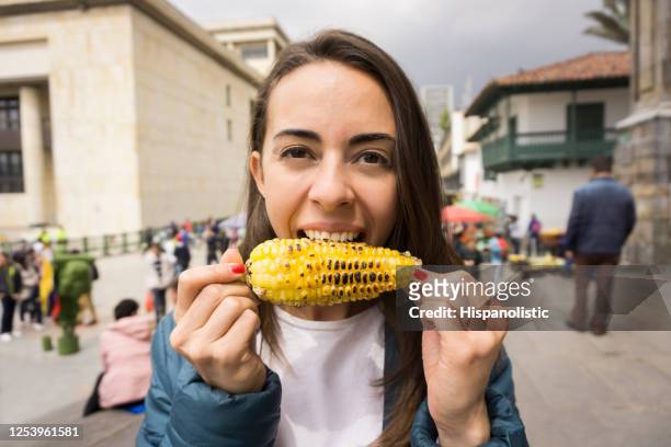 femme latino-américaine appréciant le maïs sur l’épi souriant à l’appareil-photo - corn cob photos et images de collection