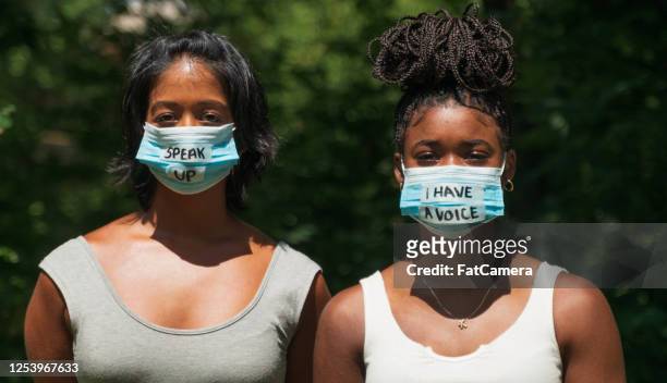 two ethnic women wear face masks with protest messages - unfairness stock pictures, royalty-free photos & images