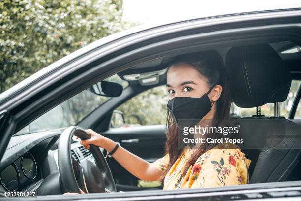 young woman  drives car during covid pandemic with protective mask - protective face mask side stock pictures, royalty-free photos & images