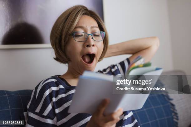 woman reading an analog book in her living room - yawning is contagious stock-fotos und bilder
