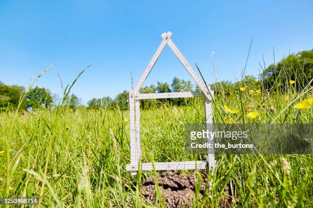 folding ruler in shape of house on a meadow against blue sky - mass unit of measurement stock-fotos und bilder