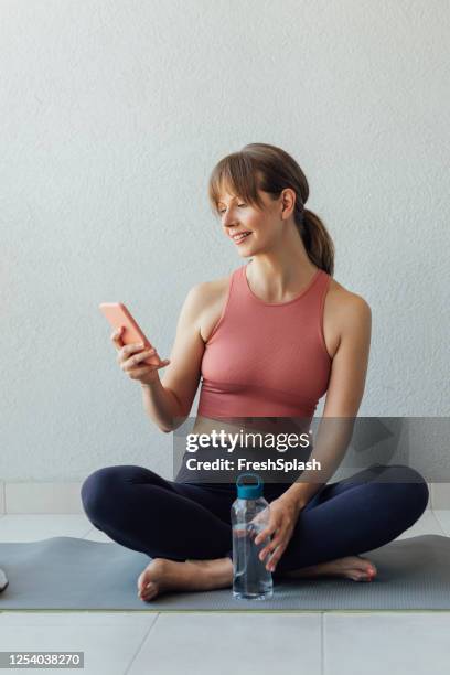 home workouts: une femme blonde happy fit choisit un programme d’exercice en ligne sur son téléphone mobile - vêtement de sport photos et images de collection