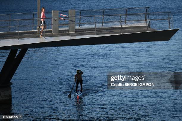 Girl runs in place on a raised drawbridge as she waits to cross a canal while a man paddles his stand-up paddleboard in Copenhagen, Denmark, on May...