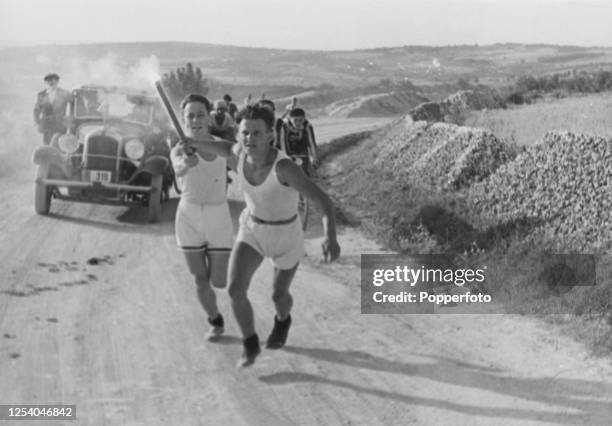 Athletes of the Sokol Organisation running with the Olympic torch along the road between Avala and Belgrade, a car and cyclists on the road behind...