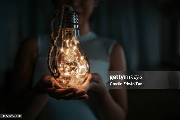 an asian chinese teenager holiding a light bulb with led light on hand in the living room on dark environment - led lighting stock pictures, royalty-free photos & images