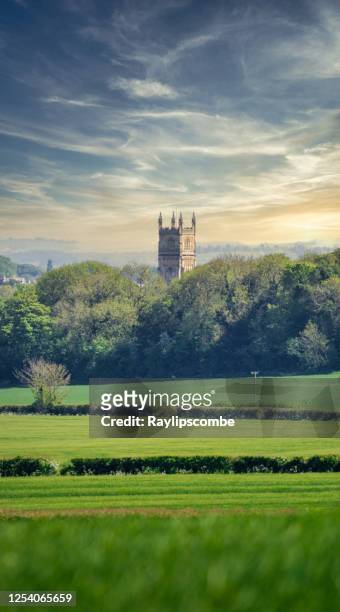 distant view of the church of st john the baptist in cirencester, gloucestershire, poking its tower above the surrounding beautiful cotswold landscape. - gloucestershire stock pictures, royalty-free photos & images