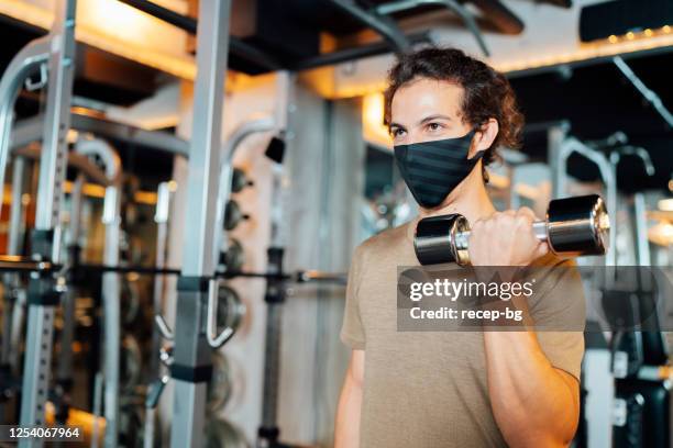 male athlete wearing protective face mask and training with dumbbell in gym - gym reopening stock pictures, royalty-free photos & images