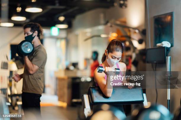 two sports persons wearing protective face masks and training in gym while keeping social distancing - health club stock pictures, royalty-free photos & images