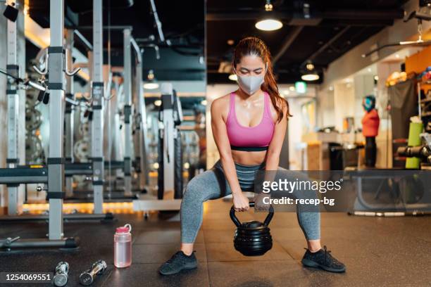 female athlete wearing protective face mask and lifting kettlebell in gym - health club stock pictures, royalty-free photos & images