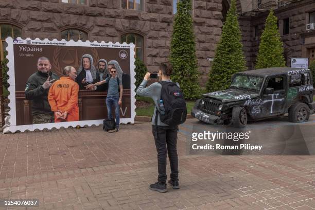 Man poses for photos in front of a poster made as a postage stamp depicting as a prisoner Russian President Vladimir Putin appearing in front of...