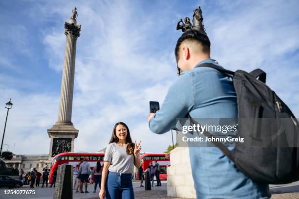smiling chinese woman making peace sign gesture for photo - trafalgar square stock pictures, royalty-free photos & images