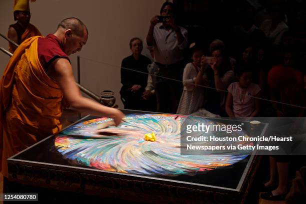 Tibetan Buddhist monk from Drepung Loseling Monastery sweeps away a mandala sand painting after millions of grains of sand are painstakingly laid...