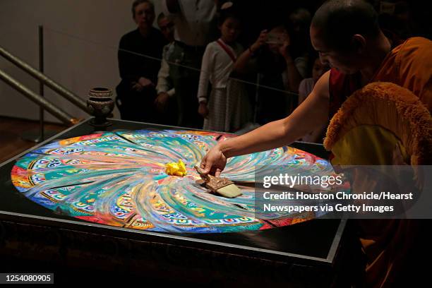 Tibetan Buddhist monk from Drepung Loseling Monastery sweeps away a mandala sand painting after millions of grains of sand are painstakingly laid...