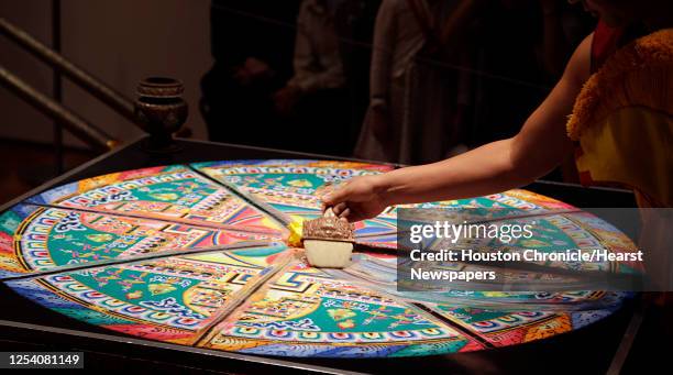 Tibetan Buddhist monk from Drepung Loseling Monastery sweeps away a mandala sand painting after millions of grains of sand are painstakingly laid...