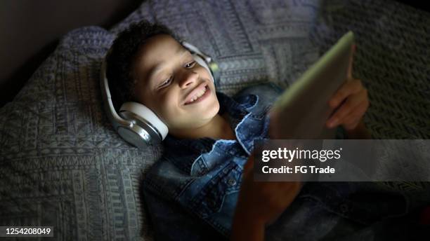 bambino che guarda un film usando un tablet digitale a letto - downloading foto e immagini stock