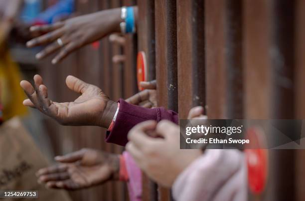 Migrants in Tijuana who have been stuck at the Mexico-United States border hold their hands out through the border fence for food from volunteers on...